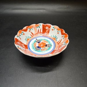 Puede incluir: Un cuenco de cerámica blanca con un borde festoneado. El cuenco está decorado con un patrón floral colorido en tonos de rojo, naranja, azul y verde.