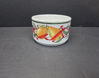 May include: White ceramic bowl with a decorative band featuring illustrations of pears, apples, red ribbons, and green leaves. The bowl has a green border around the rim. A festive design for serving food.