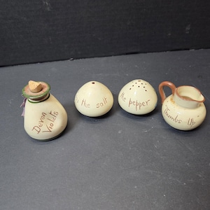 May include: A set of four ceramic kitchen items. Includes a teardrop-shaped bottle with "Devon Violets" text, two egg-shaped shakers labeled "the salt" and "the pepper", and a small pitcher with "Thumbs Up" text.