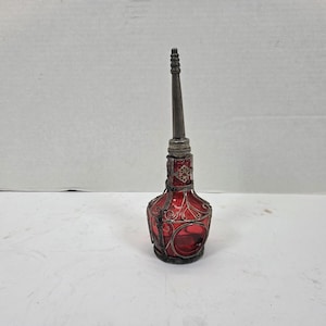 May include: A red glass perfume bottle with a silver-colored metal filigree design. The bottle has a long, slender neck and a decorative stopper. The bottle is an antique style.