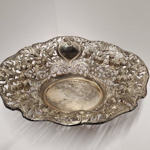 May include: A silver-plated decorative bowl with an intricate, openwork design featuring floral motifs. The bowl has a heart-shaped design in the center.