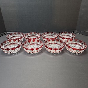 May include: A set of eight small glass bowls featuring a clear, diamond-patterned base and a vibrant red, scalloped rim. Each bowl has a textured exterior with a repeating geometric design, creating a consistent look across the entire collection.