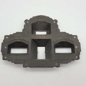 Puede incluir: Un soporte de pared de metal negro con tres aberturas rectangulares. Las aberturas tienen tapas arqueadas decorativas y están dispuestas de forma simétrica.