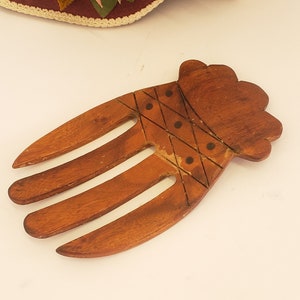 Op de afbeelding: Een houten salade-serveerschep in de vorm van een hand met vier tanden. De schep is donkerbruin en heeft een gesneden ontwerp aan de achterkant.