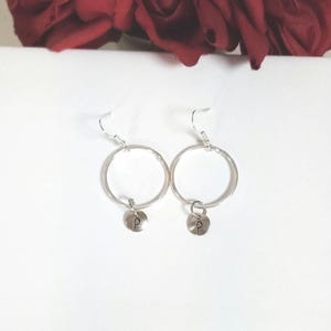 Puede incluir: Pendientes de aro de plata con un pequeño dije de plata que tiene la letra 'P'.