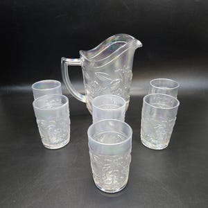May include: A set of six clear glass tumblers and a pitcher with a floral design. The glasses and pitcher have an iridescent finish.