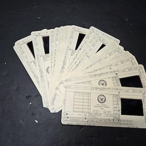 May include: A fan-shaped collection of off-white rectangular aperture cards, each featuring a central square cutout and printed technical data. The cards display the text DUAL PURPOSE ENGINEERING DOCUMENT CARD, a government seal, and various grid fields.