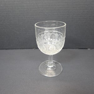 May include: Clear glass goblet with a decorative pattern on the bowl. The stem and base are also clear. The goblet is designed for serving beverages. The glass is transparent, allowing the contents to be visible.