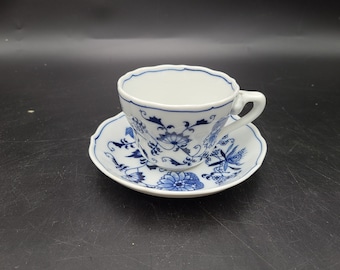May include: A white teacup and saucer with a blue floral pattern. The cup has a scalloped rim and a handle. The saucer has a scalloped edge.