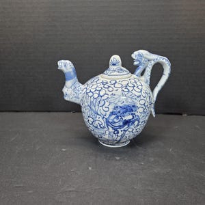 Könnte beinhalten: Eine blau-weiße Keramik-Teekanne mit einem drachenförmigen Griff und Ausguss. Die Teekanne hat ein Blumen- und Vogelmuster. Der Deckel hat einen kleinen Knopf. Die Teekanne ist ein dekorativer Gegenstand.