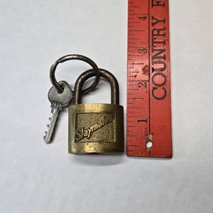 Puede incluir: Un candado de latón con una llave adjunta. El candado tiene un logotipo de Slaymaker en la parte delantera. El candado mide aproximadamente 5 cm de largo.