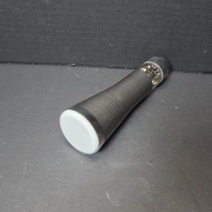 May include: A black pepper grinder with a gray base and a black top. The body of the grinder is a matte black, with a slightly textured surface. The grinder is lying on a dark gray surface.
