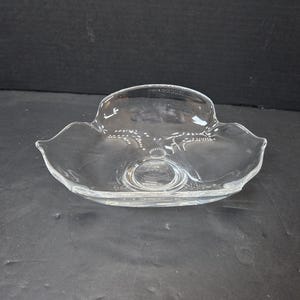 May include: A clear glass serving dish with a scalloped edge. The dish has a shallow, oval shape with a raised center and a decorative design. The glass is transparent, allowing light to pass through.