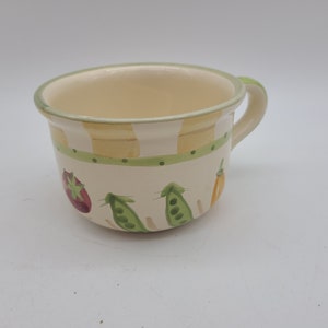 Peut inclure: Un bol à soupe en céramique blanche avec une anse verte. Le bol est décoré de rayures jaunes et vertes avec une fraise, des pois et un poivron jaune peints sur le côté.