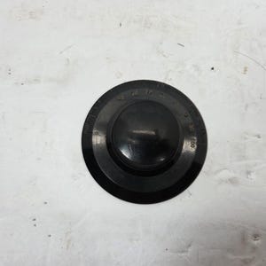 May include: A black, circular dial with a central knob and a numbered scale from 0 to 100. The dial is made of a matte material and sits on a white surface.