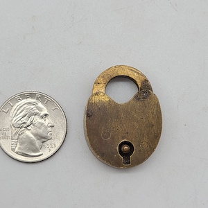 May include: A brass padlock with a keyhole and a small metal knob. The padlock is about the size of a 20 pence coin.