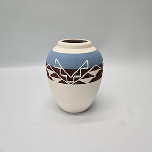 May include: A small white ceramic vase with a blue and brown geometric pattern.