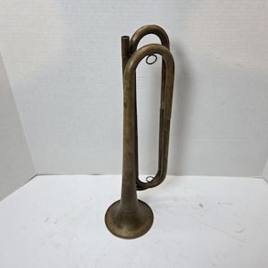 May include: A vintage brass bugle with a flared bell and curved tubing. The instrument has a tarnished finish, showing signs of age and use. The bugle is designed with a mouthpiece and a loop for a lanyard.