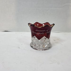 以下が含まれることがあります： 深いルビーレッドの上部に白い文字でSouvenir of Springfield, Mass.と書かれた、広がった形の小さなガラス容器。下部は透明なガラスで、ダイヤモンドカットの模様と金色の縁取りが施された波状の縁が特徴です。