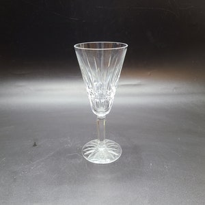 May include: A clear crystal champagne flute with a long stem and a wide, patterned base. The glass has vertical etched lines on the bowl, creating a textured appearance. The glass is approximately 23 cm tall.