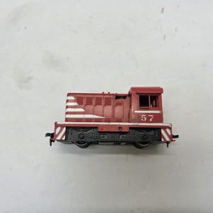 May include: A red and white model train with the number 57 on the side. The train has a detailed design with white stripes and black wheels. The model train is a miniature replica of a diesel locomotive.
