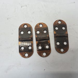 May include: Three antique copper-colored hinges with rounded ends and multiple holes for screws. The hinges are slightly tarnished, showing signs of age and use. They are likely for a small cabinet or box.