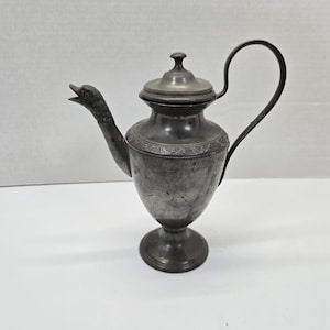 May include: A silver teapot with a bird-shaped spout and a decorative floral design. The teapot has a lid and a handle.