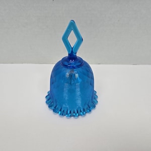 Puede incluir: Una campana de cristal azul con un asa en forma de diamante. La campana tiene una superficie texturizada y un borde festoneado.