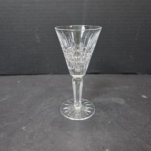 May include: A clear crystal wine glass with a detailed, cut-glass design. The glass has a conical bowl, a slender stem, and a circular base. The cut-glass pattern creates a sparkling effect, reflecting light. The glass is designed for serving wine.