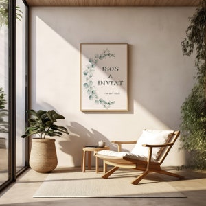 Puede incluir: Una impresión enmarcada con una ilustración de acuarela de hojas de eucalipto en tonos verdes. La impresión presenta el texto "ISOS A INVIAT" y "Marcos 7:14-15". La impresión está colgada en una pared blanca en una habitación con una silla de madera y una mesa pequeña.