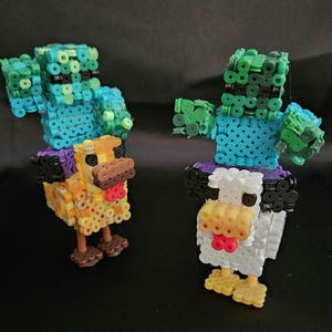 Peut inclure: Deux figurines en pixel art, l'une représentant un poulet et l'autre un zombie, fabriquées à partir de perles en plastique colorées. Le poulet est jaune, orange et marron, tandis que le zombie est bleu et vert. Les deux figurines ont les bras tendus.
