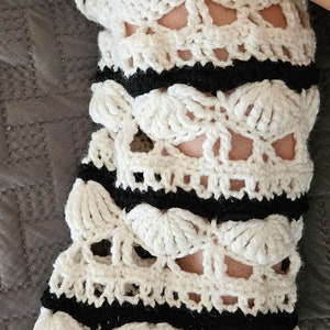 May include: White crocheted leg warmer with black trim and a skull design.