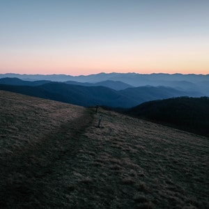 Peut inclure: Vue panoramique d'une chaîne de montagnes au crépuscule. Le ciel est d'un bleu et d'un rose doux, et les montagnes sont d'un bleu profond. Un chemin herbeux mène au sommet d'une montagne.