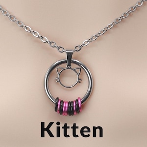 May include: A silver necklace with a cat-shaped pendant and a ring of pink and black beads. The word "Kitten" is written below the necklace, along with a morse code message.
