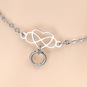 May include: Silver-toned choker necklace featuring a heart-shaped pendant with a small ring attached. The necklace has a delicate chain and is designed to be worn around the neck. The jewelry is made of metal.