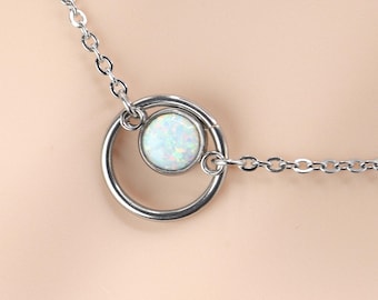 May include: A silver-toned necklace featuring a delicate chain and a circular pendant. The pendant consists of a larger silver ring framing a smaller, round, iridescent white opal-like stone set in a smooth silver bezel, creating a layered effect.