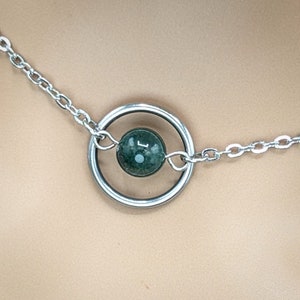 Peut inclure: Un collier en chaîne argentée avec un pendentif rond orné d'une pierre verte. Le pendentif est un cercle avec un cercle plus petit à l'intérieur, tenant la pierre.