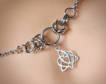 Puede incluir: Un collar de cadena de plata con un colgante de nudo celta de plata. La cadena está hecha de pequeños anillos entrelazados.