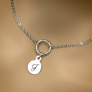 May include: A silver chain necklace with a round pendant. The pendant has a small circle at the top and a larger circle at the bottom with the letter "J" engraved on it.