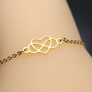 Könnte beinhalten: Ein goldfarbenes Armband mit einem zentralen Anhänger, der eine Herzform mit einem Unendlichkeitssymbol kombiniert. Der Anhänger ist mit einer zarten, dünnen Metallkette aus kleinen runden Gliedern verbunden, was ein durchgehendes Design ergibt.