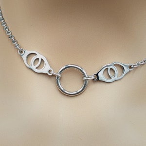 Könnte beinhalten: Eine silberne Kettenkette mit zwei offenen Kreisdesigns und einem großen silbernen Ring in der Mitte.