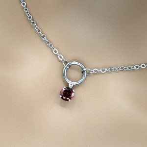May include: A silver necklace with a deep red gemstone pendant. The pendant is a small, round, red stone set in a silver setting. The pendant hangs from a silver ring, which is attached to a delicate chain.