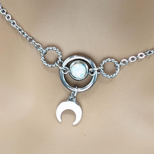 Puede incluir: Un collar de cadena de plata con un colgante circular que presenta una piedra de ópalo blanco y un dije de luna creciente.