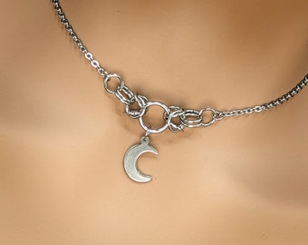 May include: A silver chain necklace with a crescent moon charm. The chain is made of multiple linked rings.