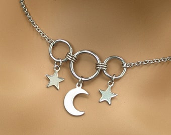 May include: A silver chain necklace with three interconnected rings and dangling charms. The charms include a crescent moon and two five-pointed stars.