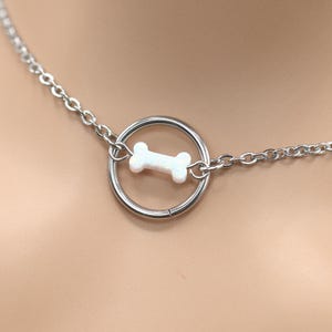 May include: A silver chain choker necklace with a circular pendant featuring a white bone charm.