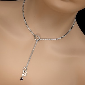 Puede incluir: Un collar de cadena de plata con un dije colgante que presenta un diseño de gato estilizado y una pequeña piedra preciosa púrpura.