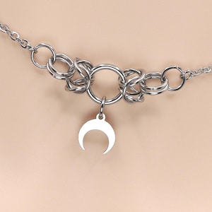 May include: A silver chain necklace with a large silver ring and a crescent moon pendant.