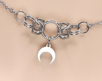May include: A silver chain necklace with a large silver ring and a crescent moon pendant.
