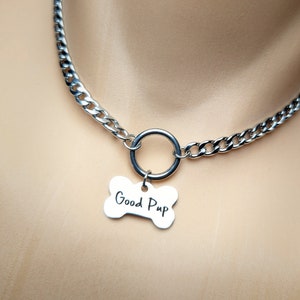 Puede incluir: Un collar gargantilla de cadena plateada con un anillo plateado y una etiqueta en forma de hueso que dice "Good Pup".